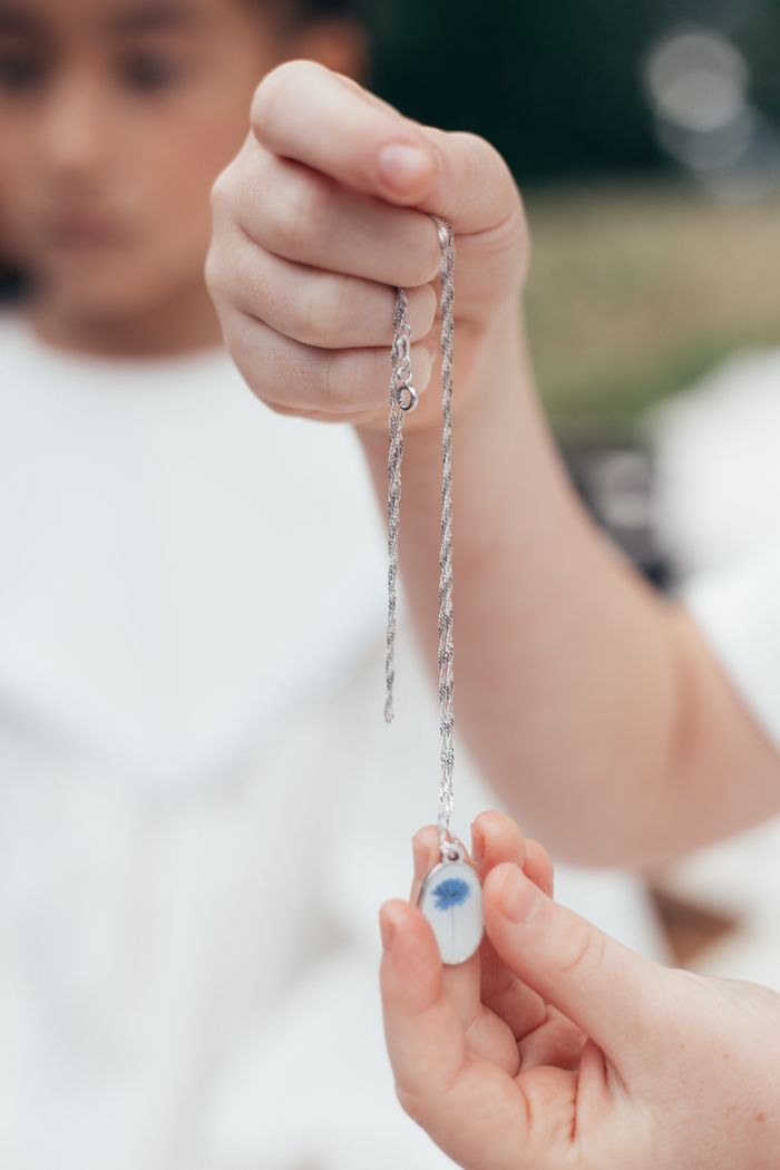 Close-up of hands holding a silver chain necklace with a blue pendant, outdoors.