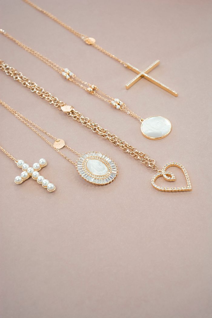 Services A collection of elegant gold necklaces and pendants artfully arranged on a soft pink background.